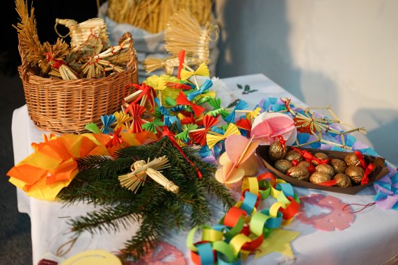 Stół z kolorowymi ozdobami świątecznymi, słomiane aniołki, łańcuchy dekoracyjne z papieru, pomalowane na złoto orzechy włoskie