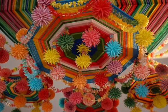 Kolorowe zdjęcie, fragment ludowego pająka, pompony z bibuły w różnych kolorach zamocowane na tkanej z włóczki tarczy