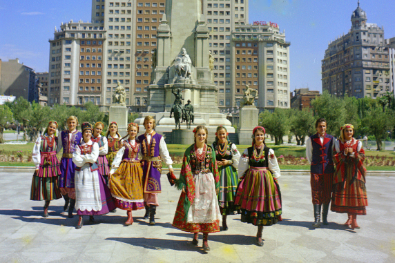 Kolorowe zdjęcie, dwanaście osób w strojach ludowych idących po Plaza de España w Madrycie