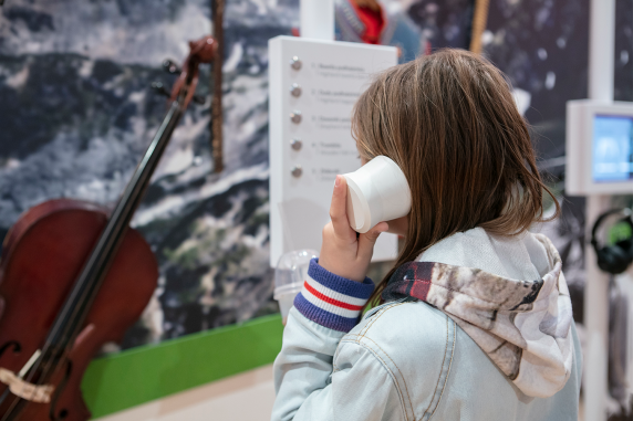 A girls holds a receiver to her ear at the exhibition in the Centre for Polish Folklore. She is standing in front of a display of instrumentss