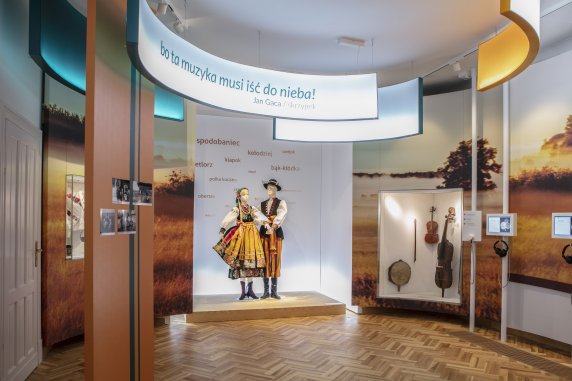 Ekspozycja z sali Mazowsze Zachodnie, na środku para manekinów w kostiumie łowickim, w gablocie po prawej instrumenty z tego regionu.